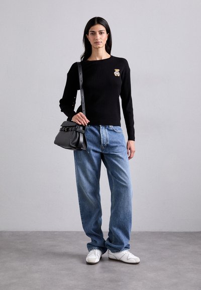 Blusa preta de manga longa canelada com um alfinete decorativo, combinada com jeans baggy azul claro e ténis brancos. Mala preta com um design estruturado.