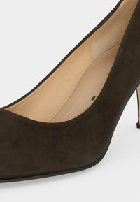 Gros plan d'une chaussure à talons hauts en daim marron foncé avec un bout pointu et une doublure intérieure beige.
