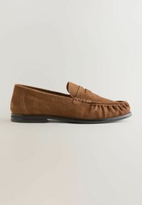 Mocassin marron en daim pour homme avec détail de bride « penny » et semelle noire, vue de côté sur fond clair.