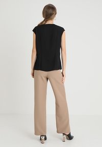Top nero a maniche corte con una texture liscia, abbinato a pantaloni beige a vita alta. Scarpe nere con tacco e accenti metallici.