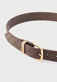 Καφέ δερμάτινη ζώνη με ανάγλυφα κυκλικά σχέδια, αγκράφα από μέταλλο χρυσού τόνου και τρύπες ρύθμισης κατά μήκος του λουριού.