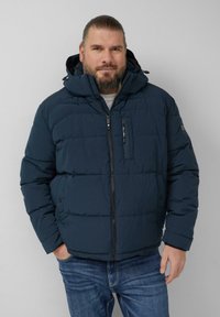 Granatowa pikowana kurtka z kapturem, z zamkiem błyskawicznym, bocznymi kieszeniami i widocznymi przeszyciami. Miękka faktura, casualowy styl. Casualowe jeansy.