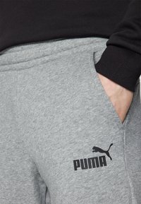 Szürke, puha anyagból készült melegítőnadrág, bal oldali zsebén fekete Puma logóval, testhezálló derékpánttal és oldalsó zsebekkel.
