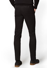 Czarne spodnie wykonane z gładkiego materiału, o dopasowanym kroju, z dwiema tylnymi kieszeniami zapinanymi na guziki oraz prostymi nogawkami.