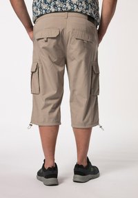 Shorts cargo beiges avec poches latérales, poignets ajustables et un matériau léger. Associés à des chaussures de sport noires et grises.