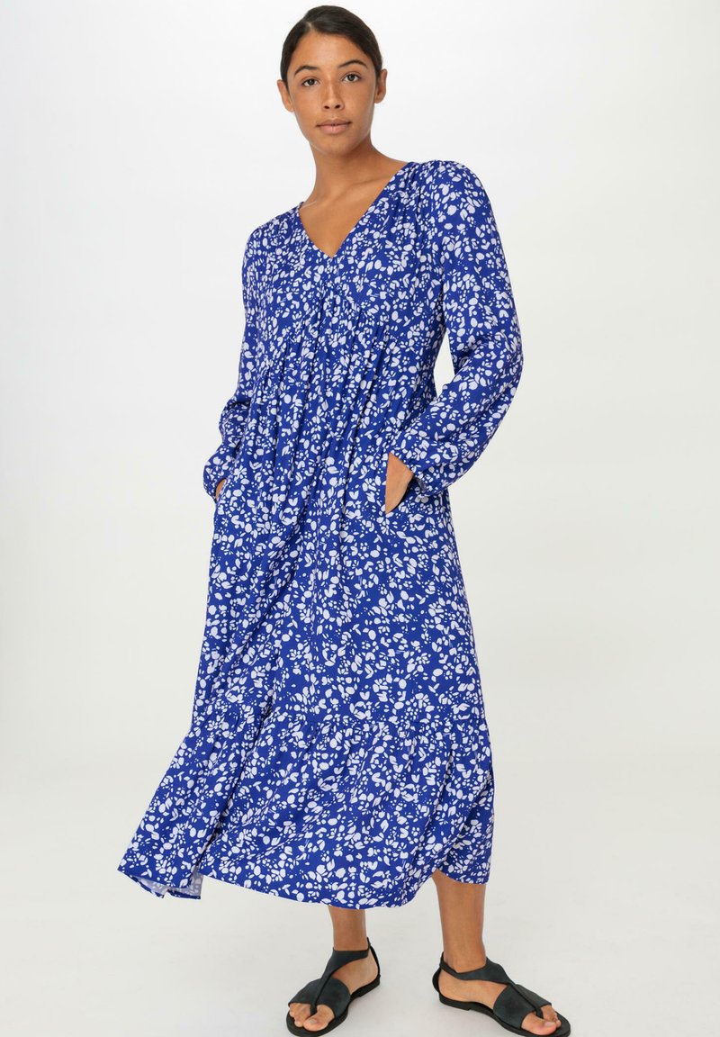 Blaues florales Langkleid mit V-Ausschnitt, langen Ärmeln, Seitentaschen und einem schwingenden Saum. Der Stoff hat eine leichte, weiche Textur.