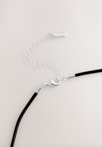 Schwarze geflochtene Kordelhalskette mit einer silbernen Metallkette und Verschluss, mit einem rechteckigen Anhänger mit geprägten Details.