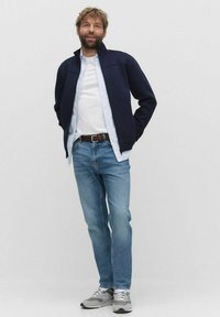 Marinblå zipjacka över en vit skjorta, ljusblå jeans och grå sneakers. Outfiten har en avslappnad design och en ledig passform.