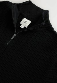 Schwarzer, strukturierter Strickpullover mit halbem Reißverschluss, geripptem hohen Kragen und sichtbarem Größenetikett M von der Marke NEXT im Kragen.