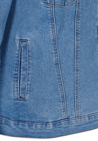 Detalj av en ljusblå denimjacka som har en sidoficka, synliga sömmar och en något texturerad tygytan. Skräddarsydd passform och rena linjer.