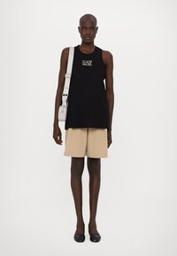 Melna bezpiedurkņu blūze ar dizainu, bēšas pielāgotas šorti un melnas plakanas kurpes. Pelēka crossbody soma ar regulējamu siksnu. Gludas audumu faktūras.