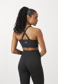 Svart sports-bh med kryssmontert stropper, glatt tekstur og logodetalj. Kombinert med høyt midje svarte leggings med subtile mønstrede akkompagnement.