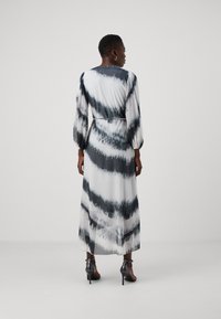 Dlouhá, splývavá šatová v bílém s tmavě šedými pruhy tie-dye. Má dlouhé rukávy, zvýrazněný pas a je doplněna vysokými podpatky.