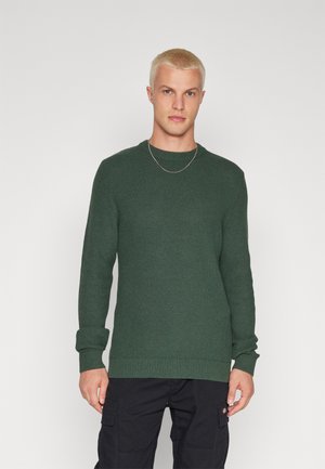 Dark green knit sweater with a textured pattern, round neckline, and ribbed cuffs and hem. Worn with black cargo pants.