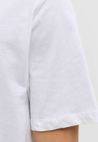 Camiseta de algodón blanca con mangas cortas, que presenta una textura simple y suave y un dobladillo enrollado en las mangas.
