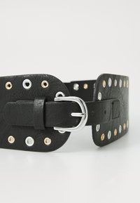Black leather belt featuring silver, gold, and white grommets along the outer edge, with a silver buckle and rectangular shape.