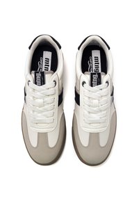 Zapatillas blancas y beiges con un acabado texturizado, que presentan detalles en negro, cordones redondos y lengüeta acolchada. Suela de goma para mayor tracción.