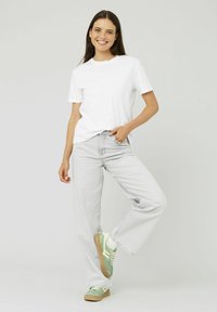 T-shirt blanc à manches courtes associé à un jean large gris clair. Le mannequin porte des baskets vert menthe avec des accents crème et une semelle beige.