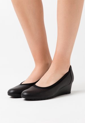 Chaussures à talon noir en forme de coin avec un bout rond, en matériau lisse. Présentent un talon bas et une bordure élastiquée à l'ouverture.