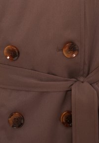 Καφέ διπλόμπουτο παλτό με δύο μεγάλα κουμπιά από χελώνιο, ζωνάκι δεμένο στη μέση και απαλό υφή.