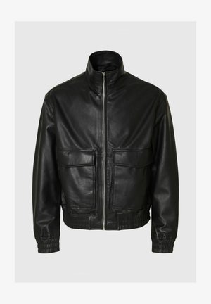 Musta nahkatakki, jossa on korkea kaulus, kaksi etutaskua läpällä, joustavat hihansuut ja vyötärö. Sileä pinta, vetoketjusuljenta edessä.