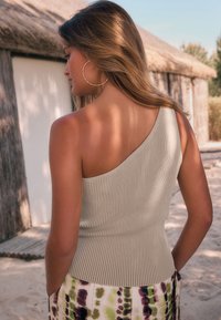 Top beige a coste con una spalla scoperta e una silhouette aderente, caratterizzato da una texture morbida e una gonna a fantasia a contrasto con elementi verdi, viola e bianchi.