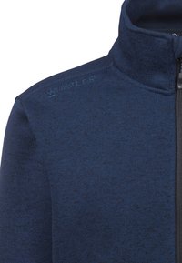 Marinblå fleecjacka med dragkedja och hög krage, texturerad tyg och en subtil melerat mönster. Har en svart dragkedja och präglat logo.