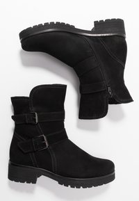 Botas de tobillo de ante negro con dos correas ajustables y hebillas. Presentan una suela texturizada y un cierre de cremallera lateral. Diseño de tacón grueso.