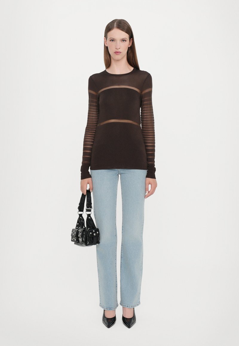 Top marrone attillato con maniche lunghe trasparenti a righe, abbinato a jeans dritti blu chiaro e una piccola borsa nera con borchie.