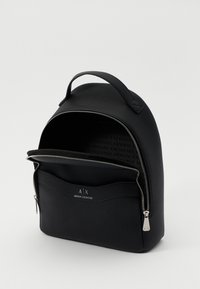 Mochila negra texturizada con forma redondeada, asa superior y acento de logo; cuenta con un cierre de cremallera y un interior espacioso.