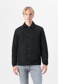 Veste noire en tissu léger avec un col plat, fermeture à boutons et poignets élastiques. Design simple sans motifs ni accents supplémentaires.