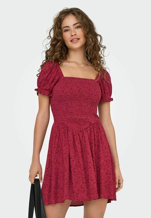 Abito rosso floreale con maniche a sbuffo, scollatura quadrata e vita arricciata. Tessuto leggero, gonna al ginocchio con una texture fluida. Borsa nera.