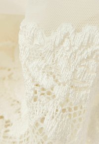 Witte kantstof met intricat bloemmotieven en een delicate nettextuur, waarbij fijne garen details langs de randen worden benadrukt.