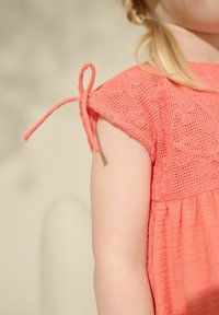 Korallenkleid mit einem strukturierten Spitzenoberteil und ausgestellt Rock. Verfügt überBindebänder an den kurzen Ärmeln und einen weichen, leichten Stoff.