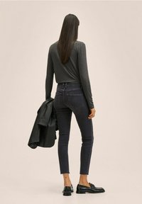 Haut à manches longues gris foncé associé à un jean foncé et des chaussures noires ; une veste en cuir noire posée sur un bras ; coupe ajustée, texture unie.