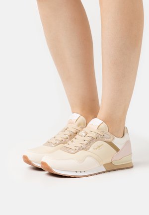 Beige sneakers, mille läikivate kuldsete detailide, tekstureeritud nööride ja pehme roosa paneeliga kannal, millel on polsterdatud tald ja logo detail.