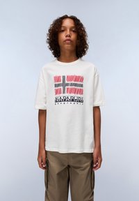 White cotton t-shirt featuring a colorful Norwegian flag graphic and "Napapijri geographic" text, paired with khaki cargo pants.