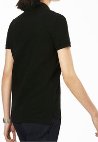 T-shirt polo noir à manches courtes avec un col, fentes latérales à l'ourlet, et texture lisse. Vue de l'arrière, montrant l'épaule et le bras.