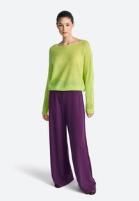 Lime zöld, laza kötésű pulóver széles nyakkivágással, széles szárú lila nadrággal párosítva. Sima textúra és kényelmes szabás.
