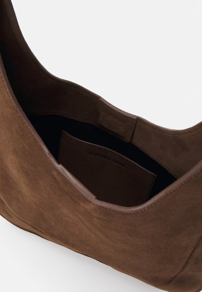 Hnědá semišová taška přes rameno s hladkým povrchem, zakřiveným otvorem a vnitřní kapsou. Minimalistický design, nevyličkovaný interiér a bezšvové okraje.