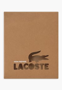 Rjava kraft papirna ovitka z izrezanim logotipom, ki prikazuje krokodila in ime blagovne znamke "LACOSTE" v pogostem, dvignjenem besedilu. Preprost in minimalističen design.