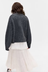 Sweater de malha cinza carvão com um corte largo e ombros caídos, sobreposto a uma saia branca, em camadas, transparente e com bordado em renda.