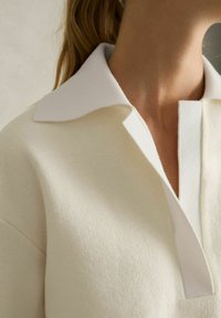 Kravefri pullover i cremefleece med en hvid, kontrasterende krave. Har et enkelt design og blød tekstur med en subtil glans.