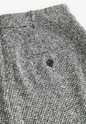 Klassikalised must-valged tekstureeritud püksid, mille vöökohal on nööpide detail, kudumise mustriga ja tagaküljel on tasku.