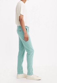 Ljust mintgröna jeans med smal passform, tillverkade av denim, som har bakfickor och en liten logotagg. Kombineras med en vit kortärmad skjorta.