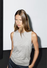 Grå ärmlös topp i mjukt tyg, med rund halsringning och avslappnad passform. Slät textur med subtila draperingsdetaljer.