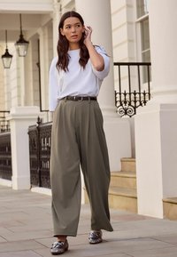 Valkoinen ylisuurikokoinen t-paita, khakinväriset leveälahkeiset housut vyöllä ja metallinhohtoiset loafersit. Sileä kangas, rento istuvuus ja minimaalinen koristelu.