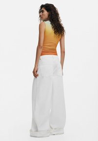 Ärmelloses Top mit Orange- und Blautonverlauf, kombiniert mit locker sitzenden weißen Denim-Hosen, die über Gesäßtaschen und umgeschlagenen Säumen verfügen.