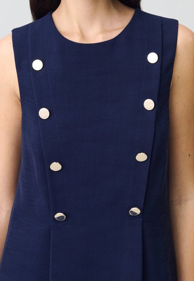 Vestido sin mangas de color navy con tejido texturizado, que presenta seis botones metálicos circulares a lo largo del lado izquierdo para el cierre y el detalle de diseño.