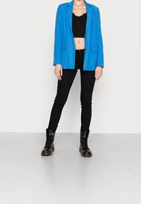 Světlý modrý blazer s dvěma předními kapsami, černý crop top, černé úzké džíny a černé šněrovací boty. Hladká textura a přiléhavý design.